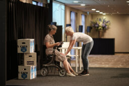 Theater A la Carte speelt een voorstelling over honderd jaar gehandicaptenzorg voor Middin. Een begeleider buigt zich voorover naar een cliënte op een rollator om echt contact te krijgen